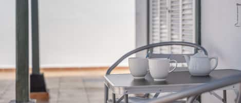 A metal table with two white cups and a teapot on a balcony.