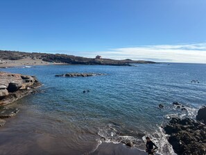 Un paysage côtier avec des rivages rocheux, une eau d’un bleu limpide et un bâtiment situé au loin, sur une colline.