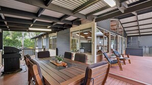 Een terras buiten met een houten tafel en stoelen, een barbecue en uitzicht op de omgeving.
