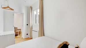 Une chambre à coucher avec un lit, un porte-manteau en bois, un radiateur et une porte donnant sur une autre pièce.