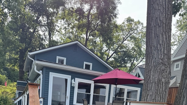 Une terrasse en bois avec un parasol rouge, une table à manger et des chaises.