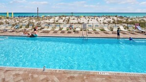A swimming pool with lounge chairs and a view of the beach.