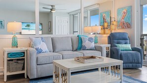 A living room with a grey sofa, a white coffee table, a blue armchair, and a large mirror.