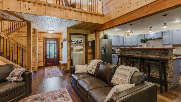 A spacious living area with a high ceiling, wooden beams, a leather sofa, and a kitchen with stone countertops.