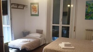 Une chambre avec deux lits simples, une chaise, un radiateur et une porte donnant sur une autre pièce.