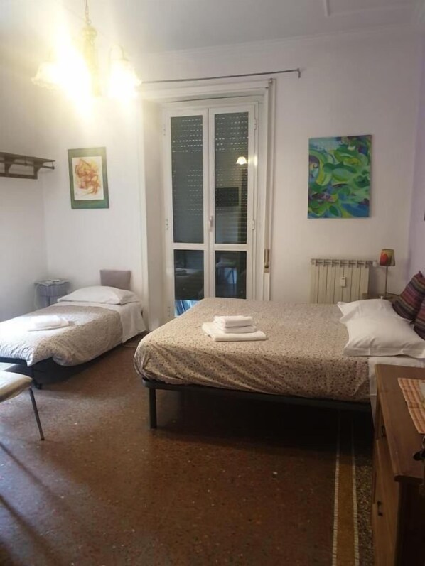 A room with two single beds, a radiator, a painting, and a door with frosted glass panels.