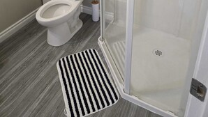 Un baño con inodoro, ducha con puerta de cristal y un felpudo a rayas en el suelo.