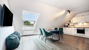 A modern loft apartment with a dining area, kitchen, and a large window with a view. - Holiday Apartment with View of Jever Castle (Jever)