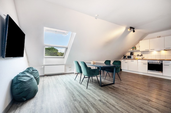 A modern loft apartment with a dining area, kitchen, and a large window with a view.