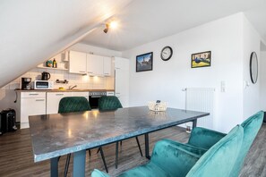 A modern kitchen with white cabinets, a dining table with chairs, and a small seating area with a sofa.