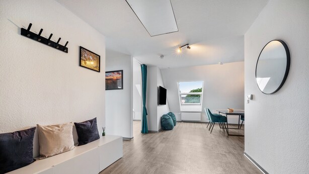 A modern interior with a sofa, a flat-screen TV, a dining area, and a large window. - Holiday Apartment with View of Jever Castle (Jever)