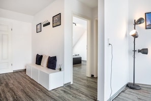 A modern interior with a white bench, a floor lamp, and a staircase leading to another room. - Holiday Apartment with View of Jever Castle (Jever)