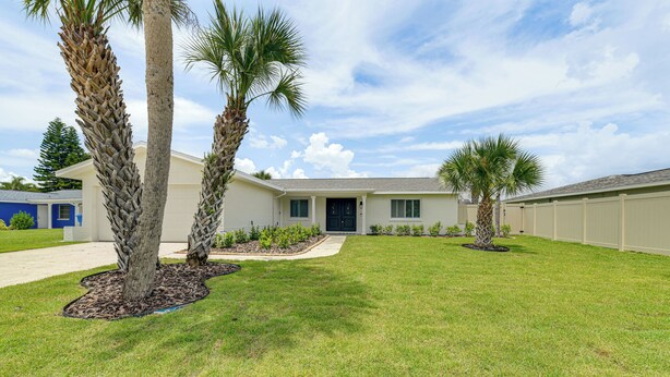 A two-story house with a front lawn, palm trees, and a clear sky. - Private Pool w/ Canal Views: Apollo Beach Getaway (Apollo Beach)
