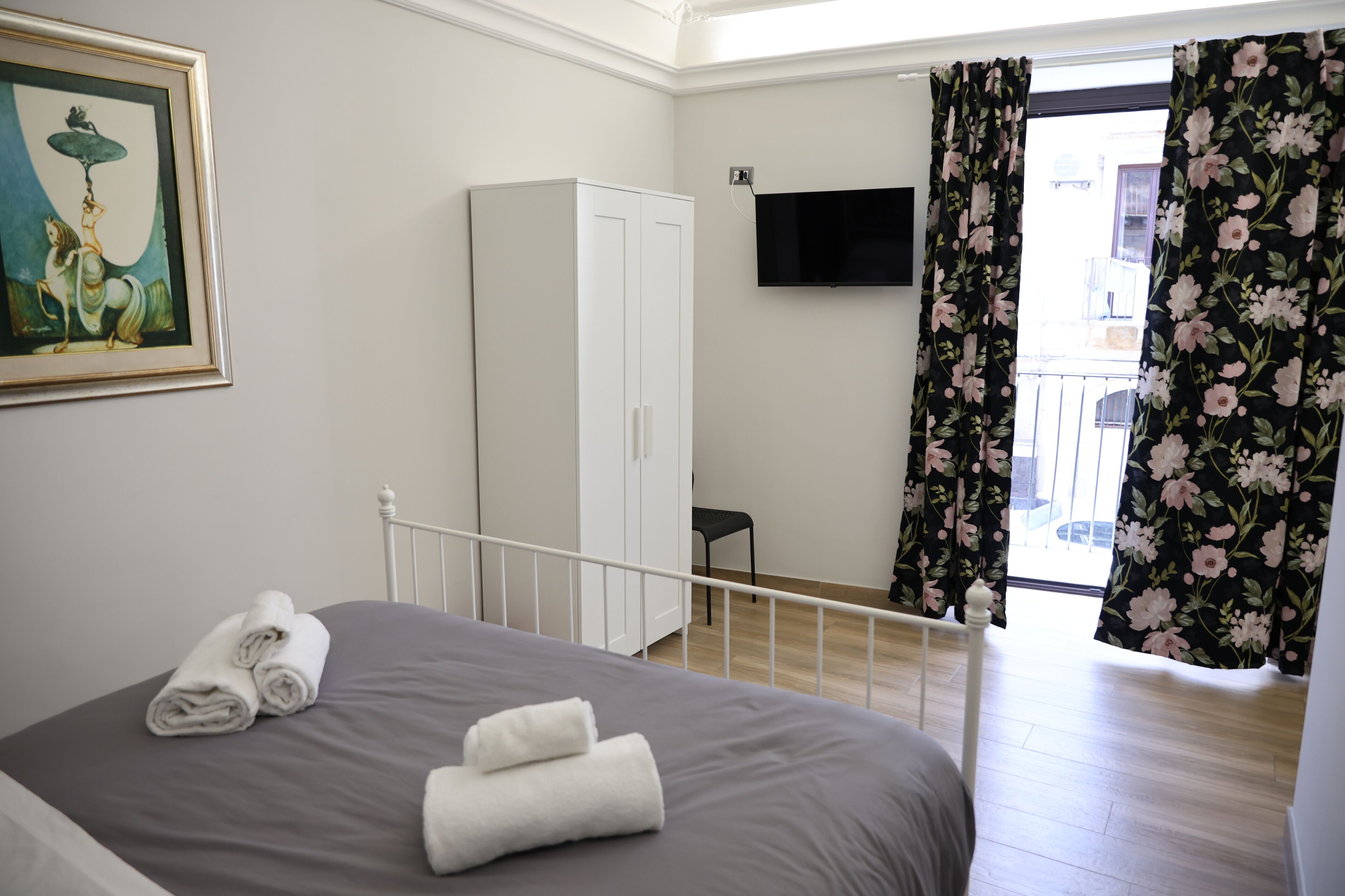 Une chambre à coucher comprenant un lit, une armoire, un téléviseur à écran plat et un balcon agrémenté de rideaux à motifs floraux.