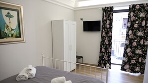 Une chambre à coucher comprenant un lit, une armoire, un téléviseur à écran plat et un balcon agrémenté de rideaux à motifs floraux.