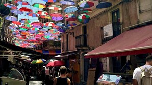 Une rue où des parapluies colorés sont suspendus au-dessus des passants.