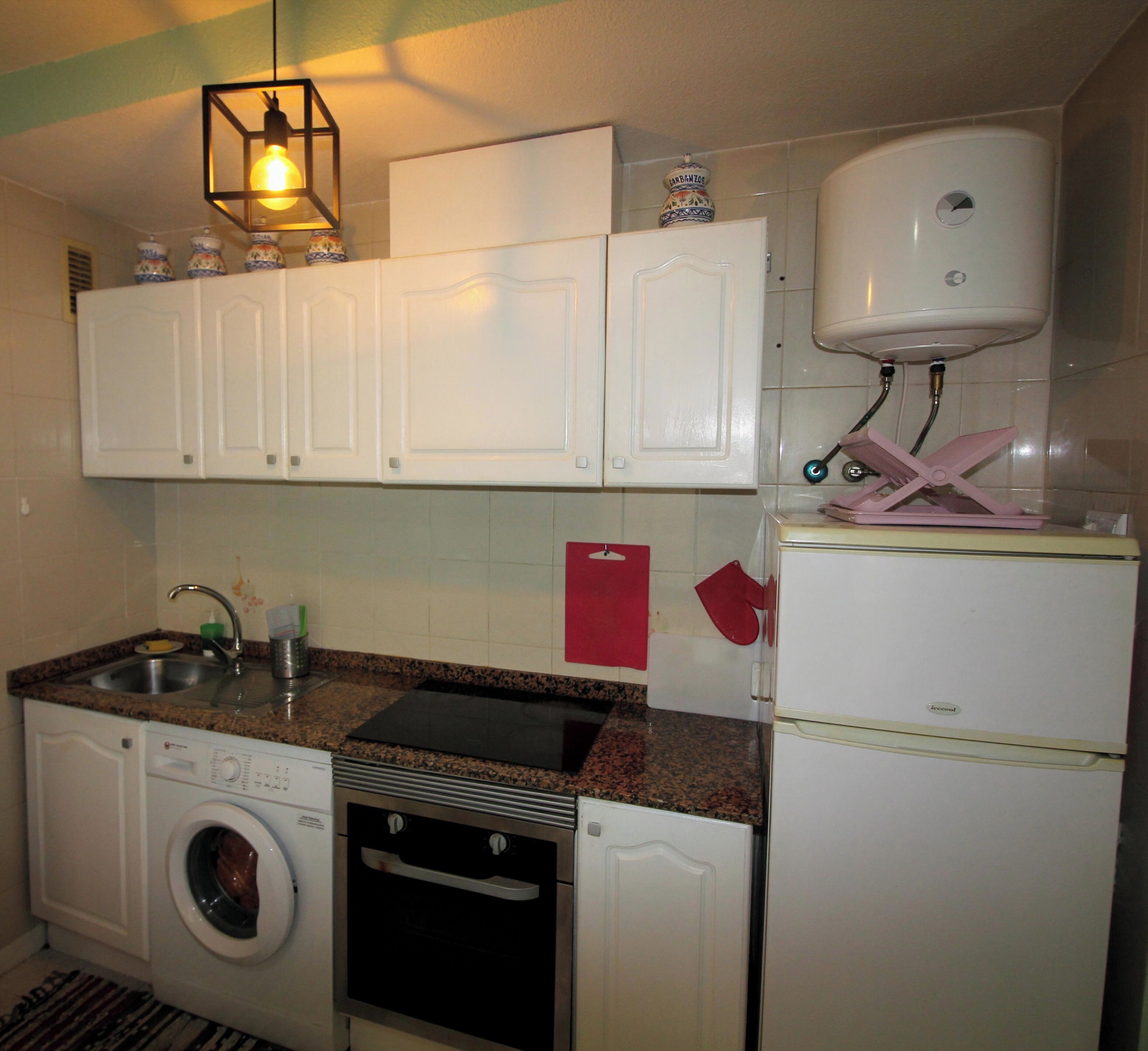 A compact kitchen with white cabinets, a washing machine, a stove, and a refrigerator.