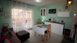 Un espace de vie compact comprenant un coin repas, une kitchenette et un canapé avec des coussins.