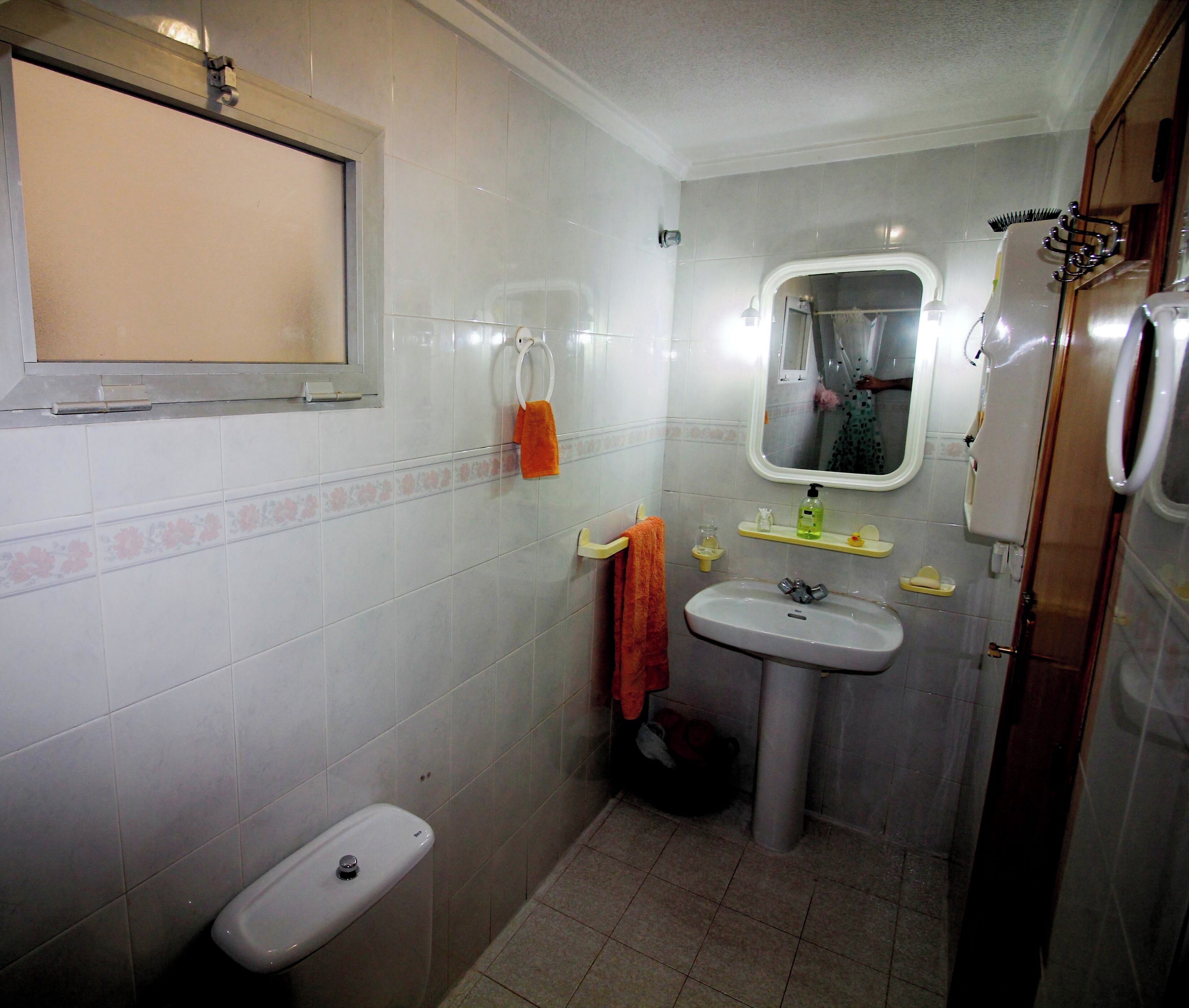 A bathroom with a toilet, sink, mirror, and shower area.