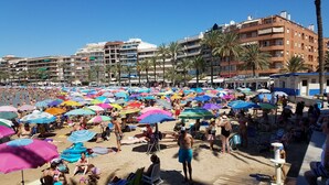 Une plage bondée, avec de nombreux parasols colorés et des gens qui prennent un bain de soleil.