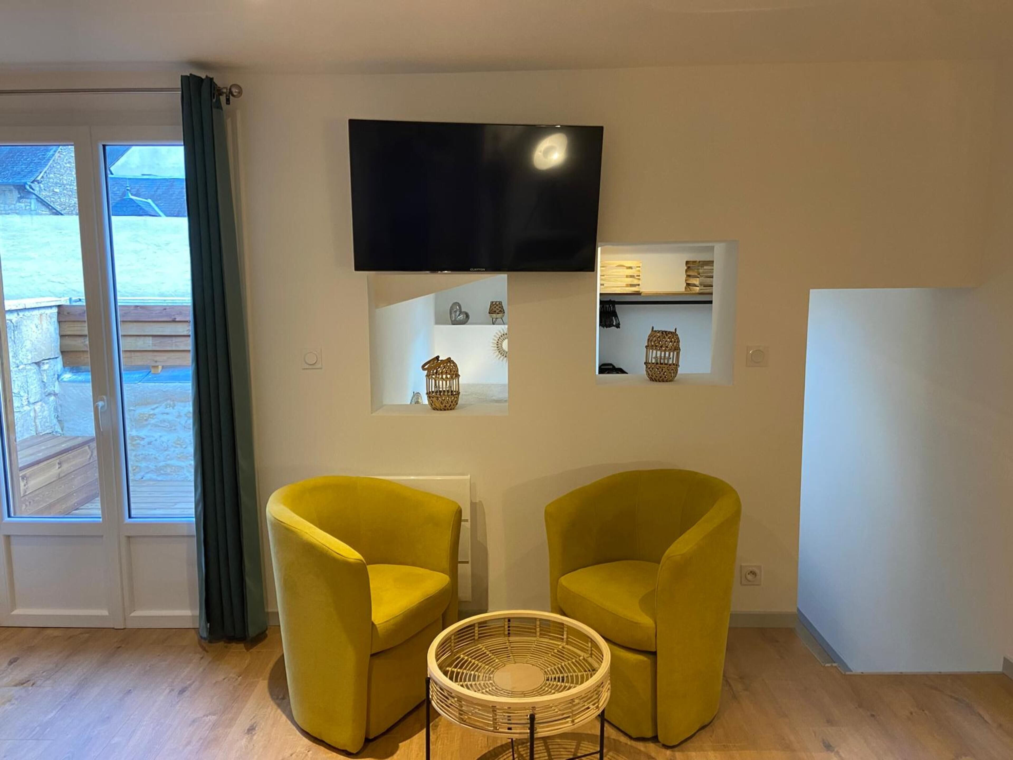 A modern living room with two yellow armchairs, a flat-screen TV, and a small side table.