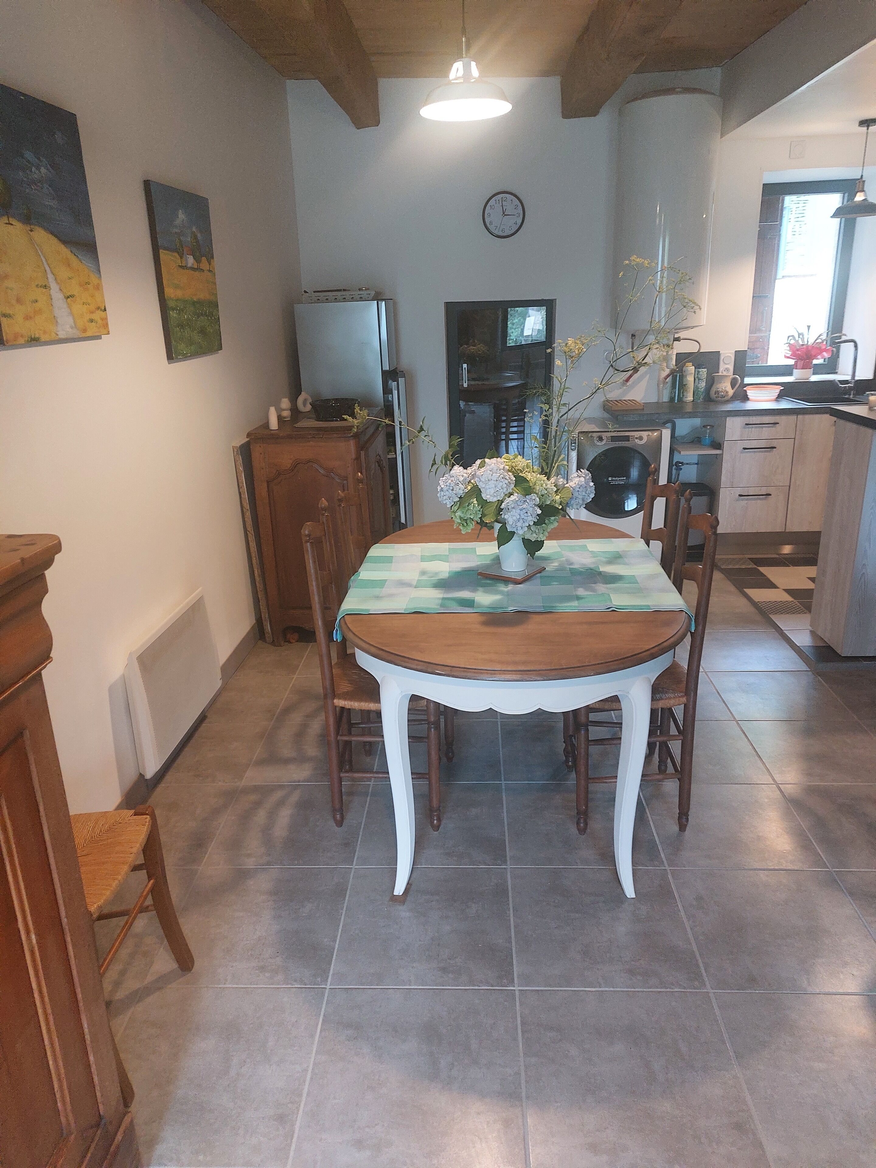 A dining area with a table set for four, a clock on the wall, and a kitchen in the background.