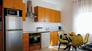 A compact kitchen with a refrigerator, oven, microwave, and dishwasher. There is a dining area with a table and chairs.