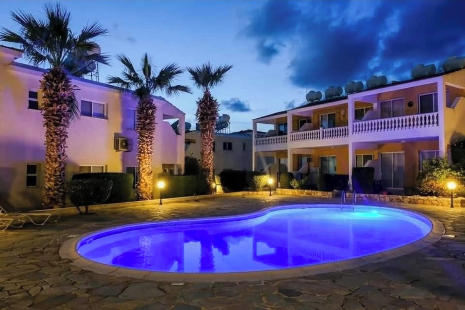 A pool area with a circular pool, palm trees, and a building with balconies.