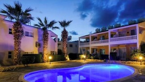 A pool area with a circular pool, palm trees, and a building with balconies.