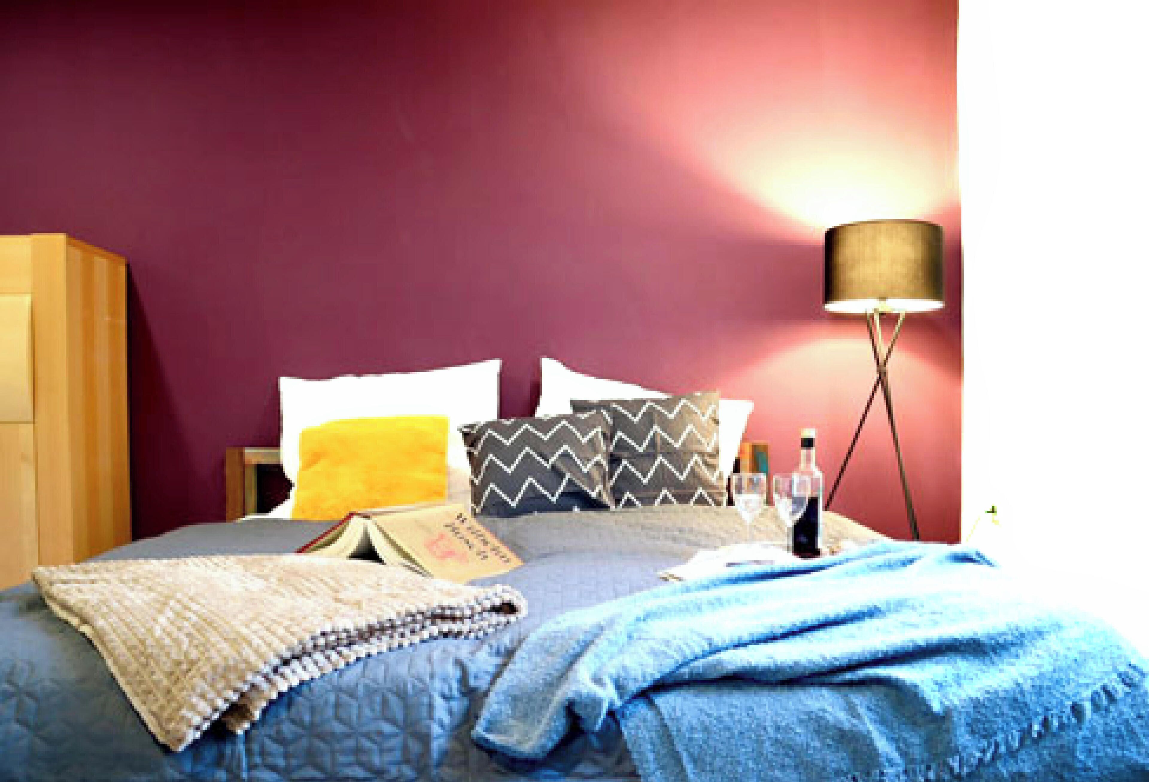 Quarto com cama, almofadas, luminária e mesa de cabeceira com garrafa e copos.