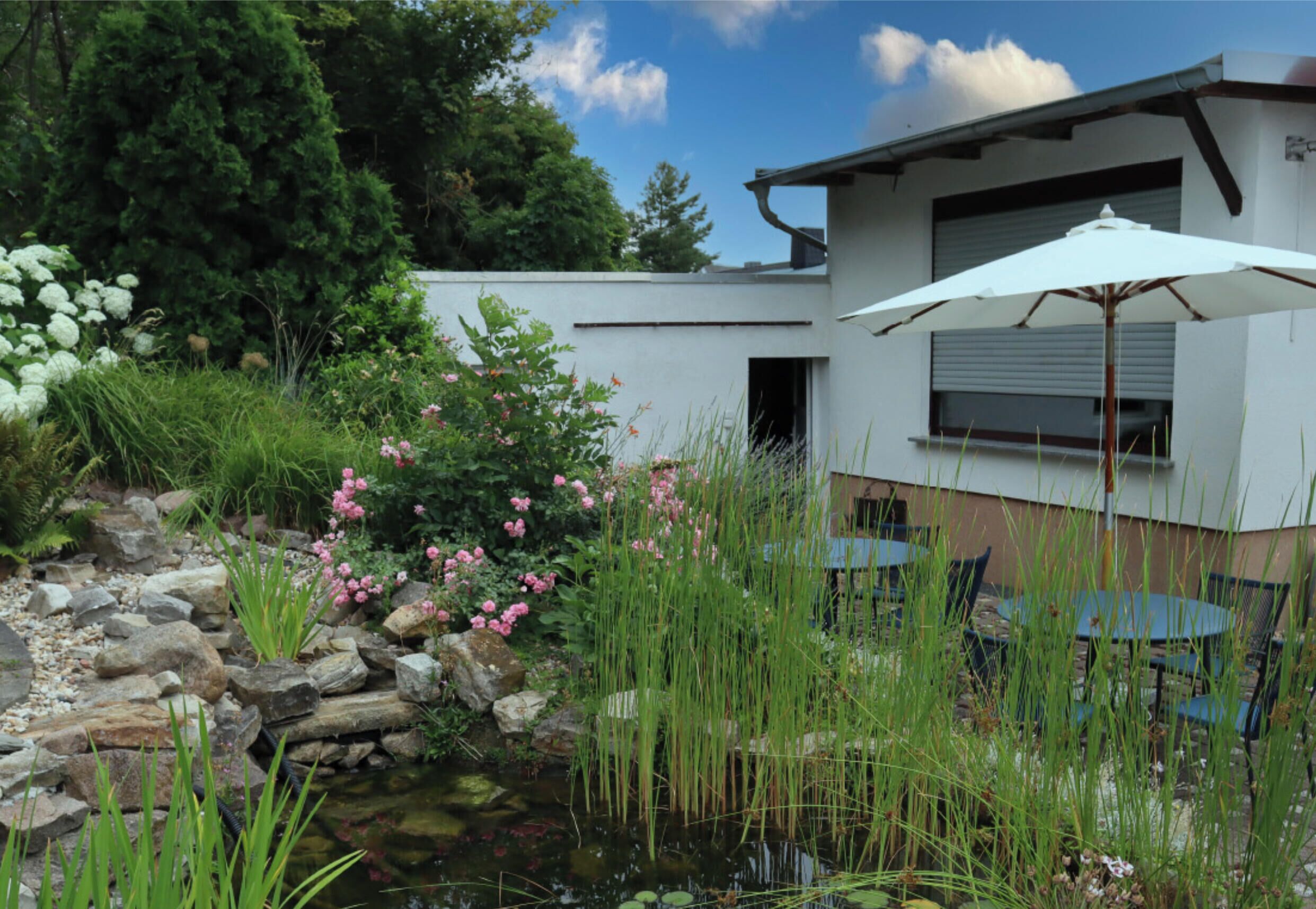 A modern house with a garden, a pond, and outdoor furniture.