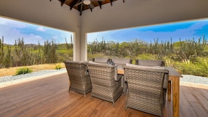 A covered outdoor dining area with wicker furniture and a view of a desert landscape. - Picaron Villas in Santa Cruz (Santa Cruz)