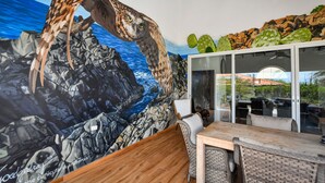 A mural of an owl on a rocky cliff with a blue ocean background, a dining area with wicker furniture, and a cactus display. - Picaron Villas in Santa Cruz (Santa Cruz)