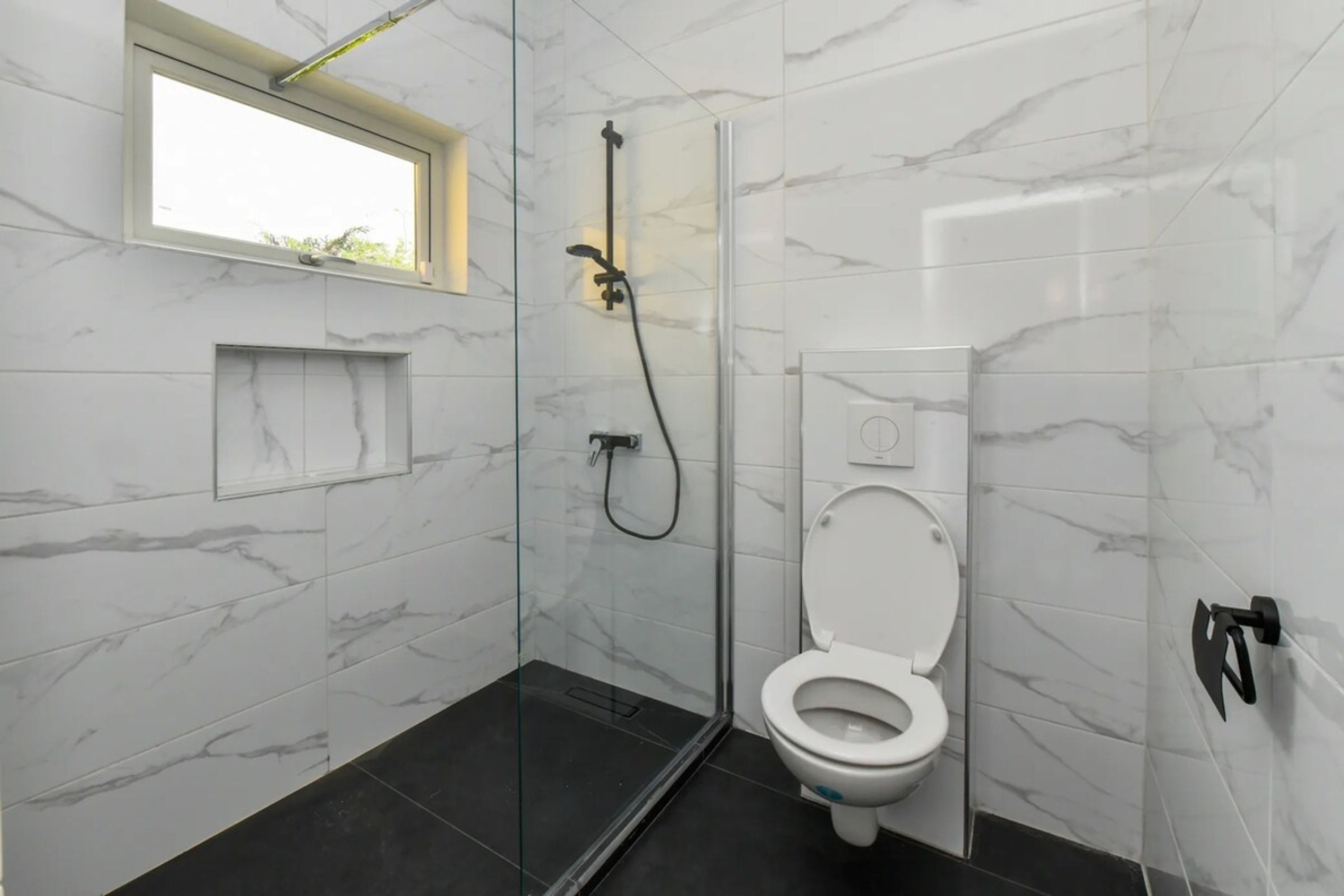 A modern bathroom with a glass-enclosed shower, a toilet, and a small window.