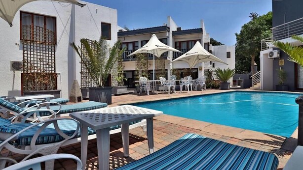 A pool area with lounge chairs and umbrellas, surrounded by buildings with balconies and potted plants. - Khayalami Hotel Mbombela (Mbombela)
