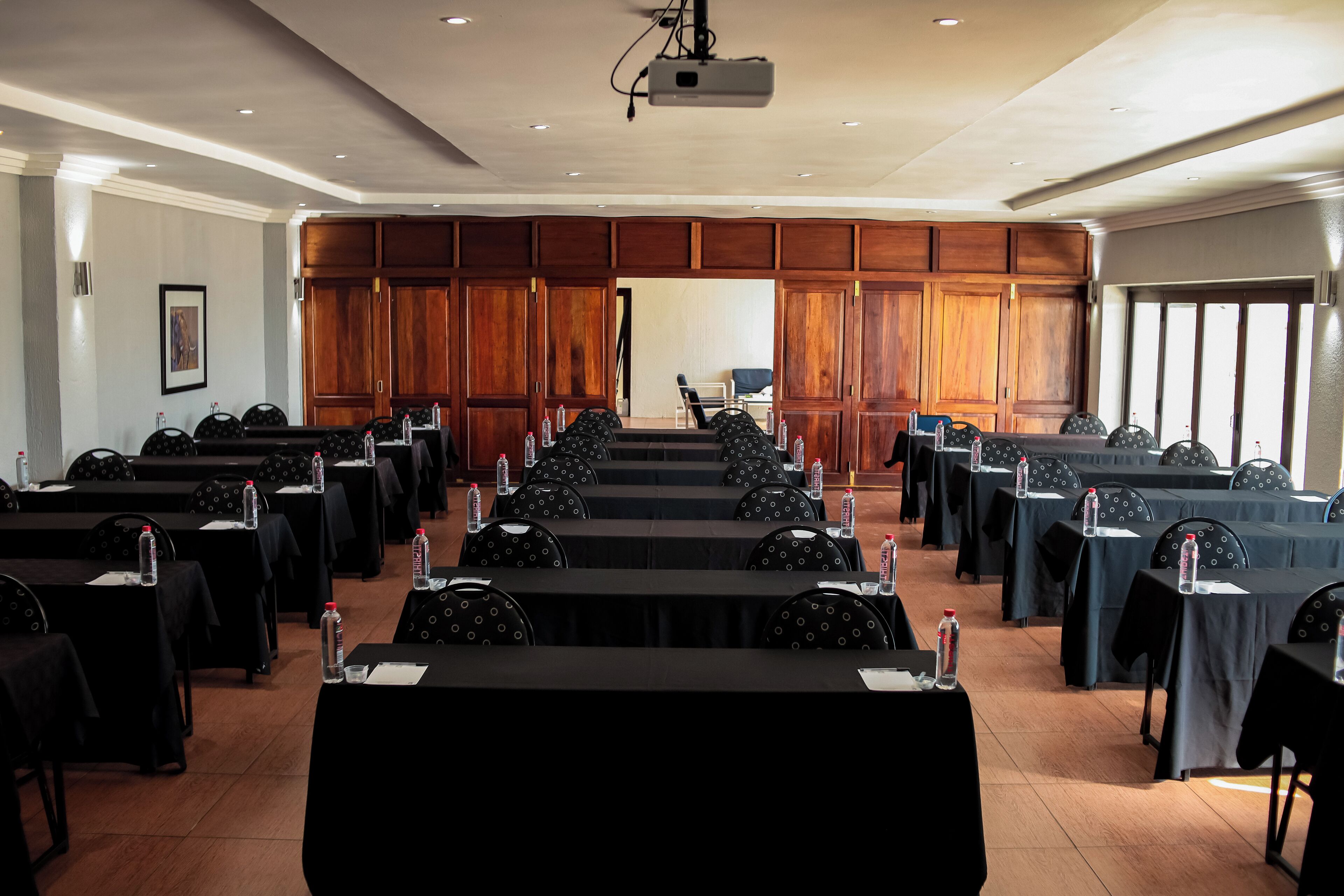 A conference room with rows of tables and chairs, equipped with water bottles and a projector.
