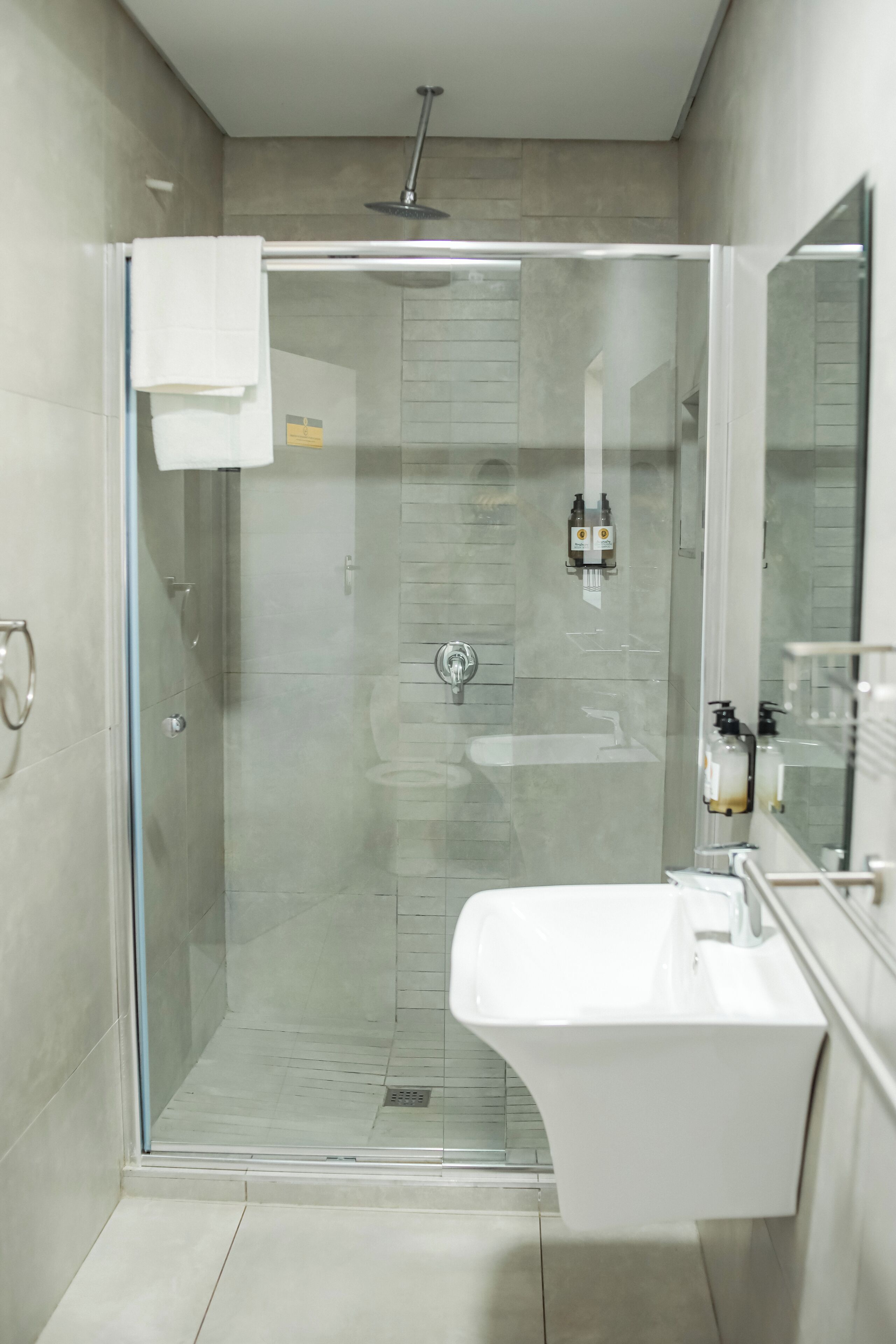 Un bany modern amb dutxa separada per vidre, un lavabo blanc i un mirall gran.