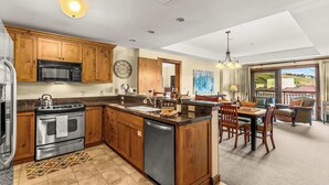 A spacious kitchen with wooden cabinets, a stainless steel stove, and a dishwasher. There is a dining area with a table and chairs, and a view of the outdoors through large windows. - NEW LISTING | beautiful 1 Bedroom with Full mountain views! (Crested Butte)