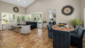 A spacious living area with a high ceiling, a dining table set for four, and a kitchen in the background. - SRC81 - 3 BD / 2 BA, 1591 sf - Remodeled Chapala! (La Quinta)