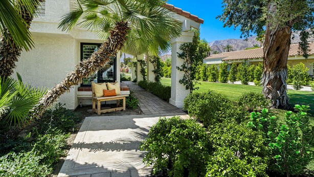 A well-maintained outdoor patio area with a wooden bench, palm tree, and lush greenery. - SRC81 - 3 BD / 2 BA, 1591 sf - Remodeled Chapala! (La Quinta)