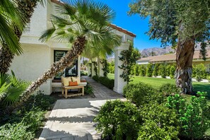 A well-maintained outdoor patio area with a wooden bench, palm tree, and lush greenery. - SRC81 - 3 BD / 2 BA, 1591 sf - Remodeled Chapala! (La Quinta)