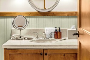 Une salle de bain équipée d’un lavabo, d’un miroir, d’une serviette, de distributeurs de savon et d’une porte.