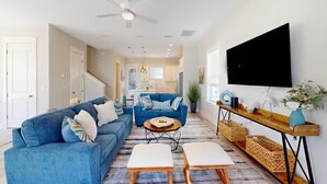 A spacious living room with a blue sofa, a coffee table, and a TV mounted on the wall.