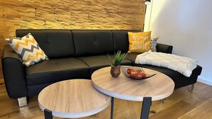 Een moderne woonkamer met een zwarte leren bank, twee ronde houten tafels en een potplant.