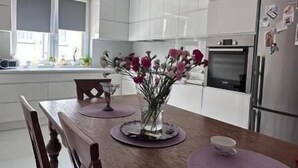 A modern kitchen with white cabinets, a wooden dining table with chairs, and a vase of flowers. - La Perla (Międzyzdroje)