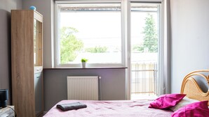 A bedroom with a bed, a window, a radiator, a wardrobe, and a plant. - La Perla (Międzyzdroje)
