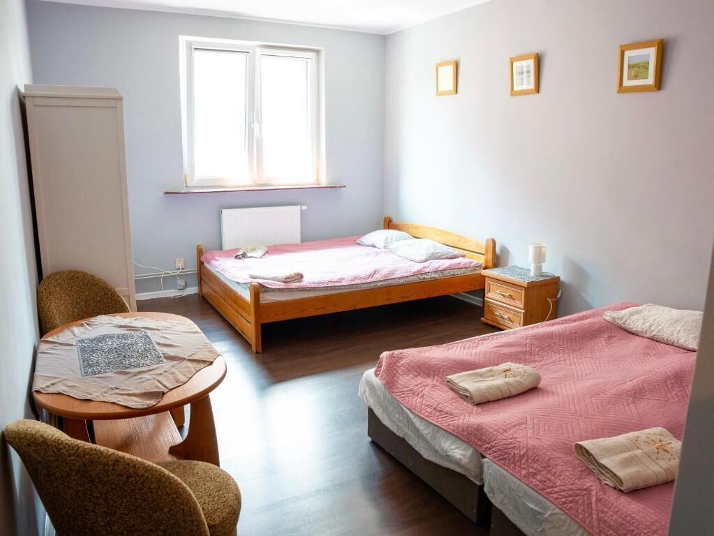 A bedroom with a single bed, a small table with chairs, a radiator, and a window.