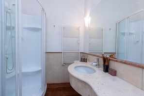 A bathroom with a glass-enclosed shower, a sink with a marble countertop, and a mirror with a wooden frame. - Rental in Rome Baccina Apartment (Rome)