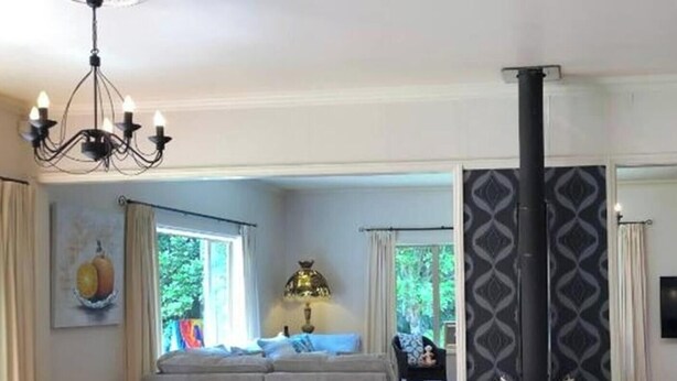 A living room with a fireplace, a chandelier, a television, and a sofa. - Serene Whangarei Lifestyle Luxurious Modern Home With Trees and Garden Views (Glenbervie)