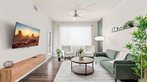 A modern living room with a flat-screen TV, a ceiling fan, a green sofa, two armchairs, a coffee table, and a potted plant. - Charming Tempe 1BR Designer Furnishings, Patio & Gym (Tempe)